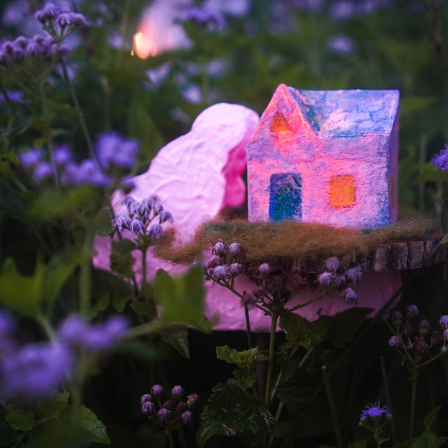 sculptural  handmade glowing house in a garden with flowers